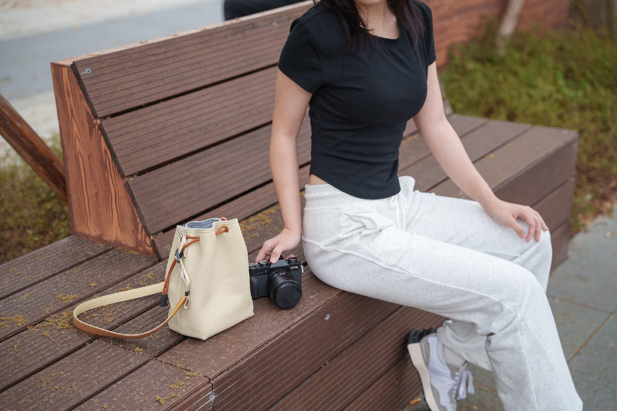 Woman on a bench with a TTArtisan cream drawstring bag and a camera
