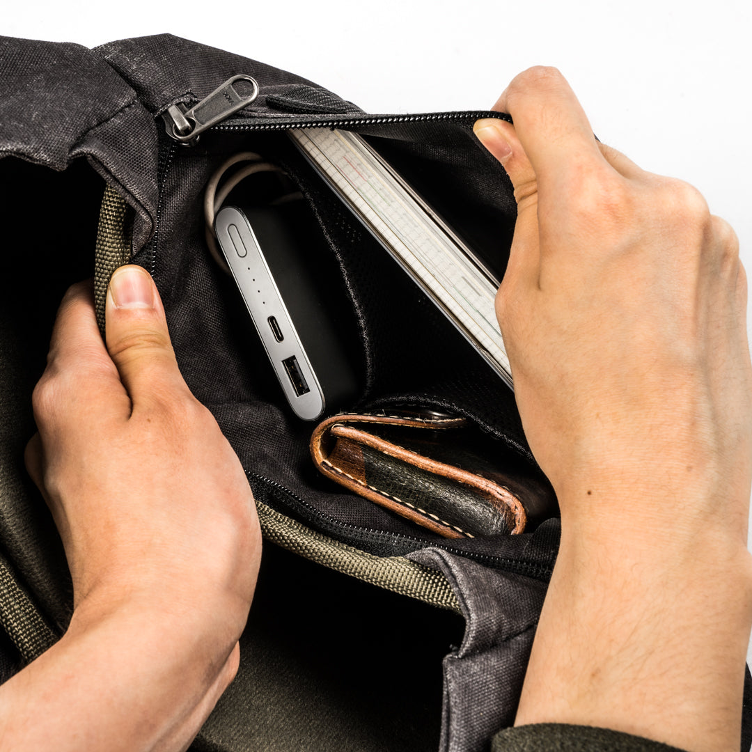 Hands opening the Wotancraft Pilot 7L inner zip pocket with power bank and wallet
