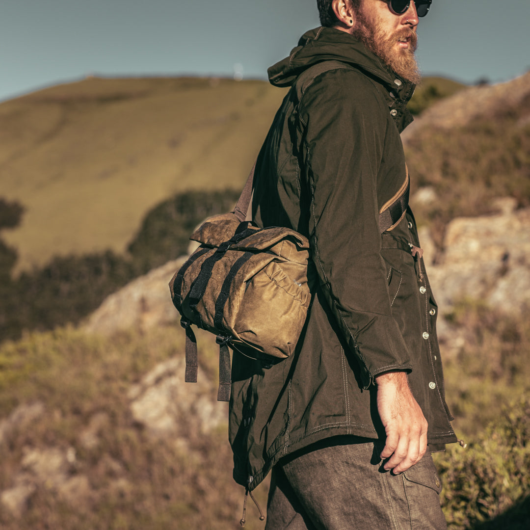 Man with a beard carrying the Wotancraft Pilot 7L khaki bag on a hillside