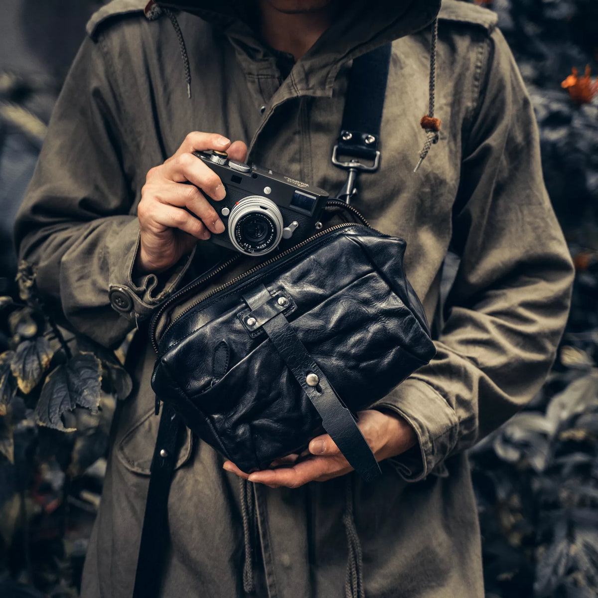 Person holding a Leica camera with the Wotancraft Mini Rider black leather sling