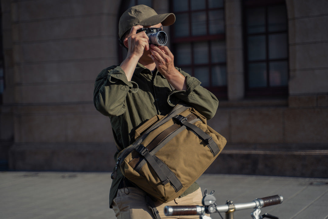 Man taking a photo with a film camera while carrying the Wotancraft Lightning Rider khaki bag