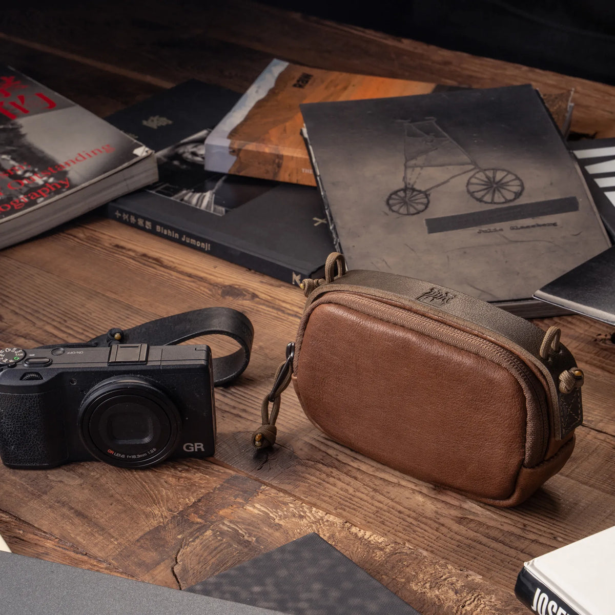 Wotancraft brown leather small pouch next to a Ricoh GR on a desk with photo books