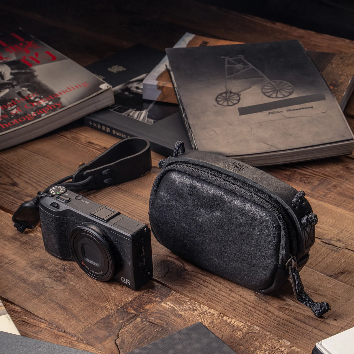 Wotancraft black leather small pouch next to a Ricoh GR on a desk with photo books