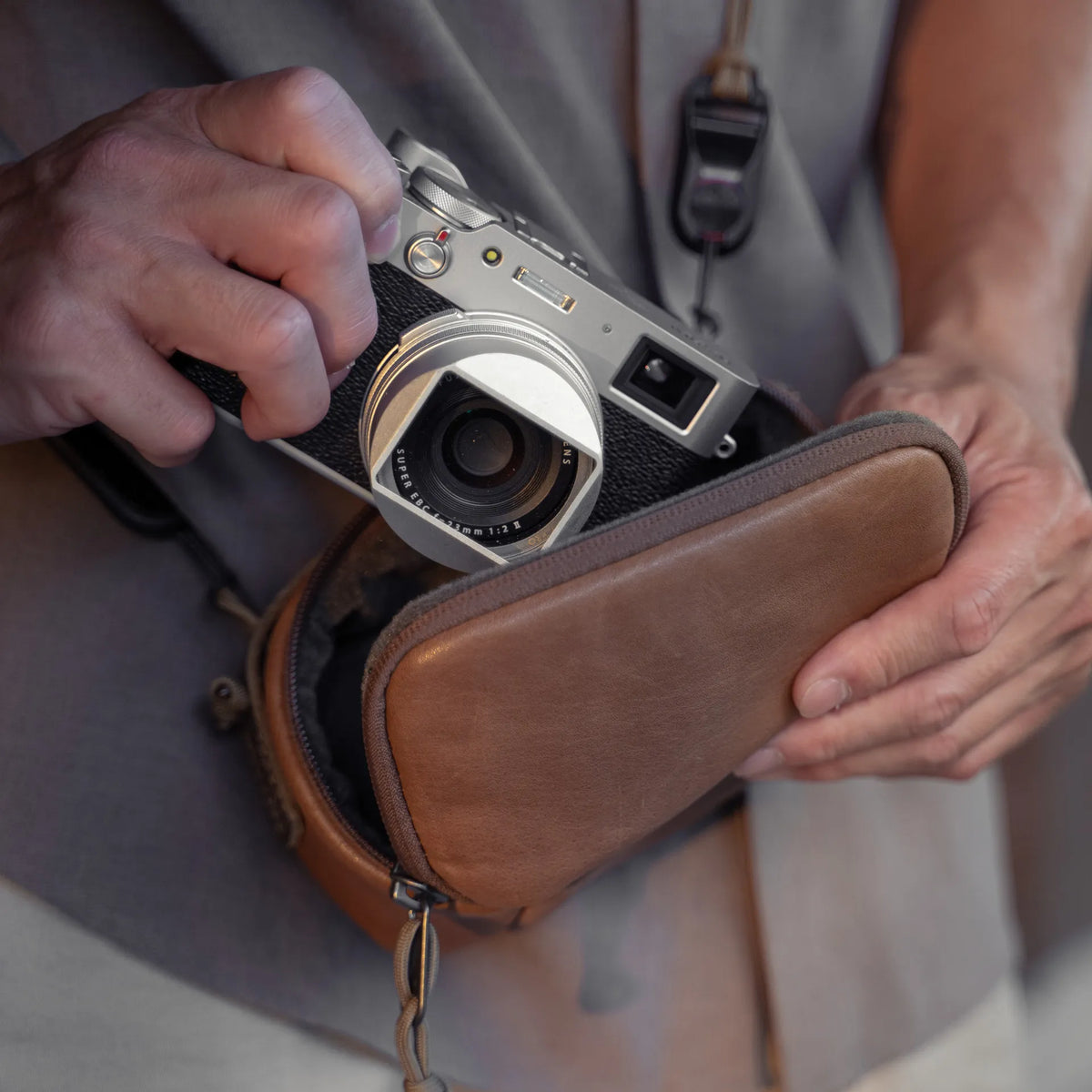 Hands taking a Fujifilm X100 out of the Wotancraft brown leather pouch