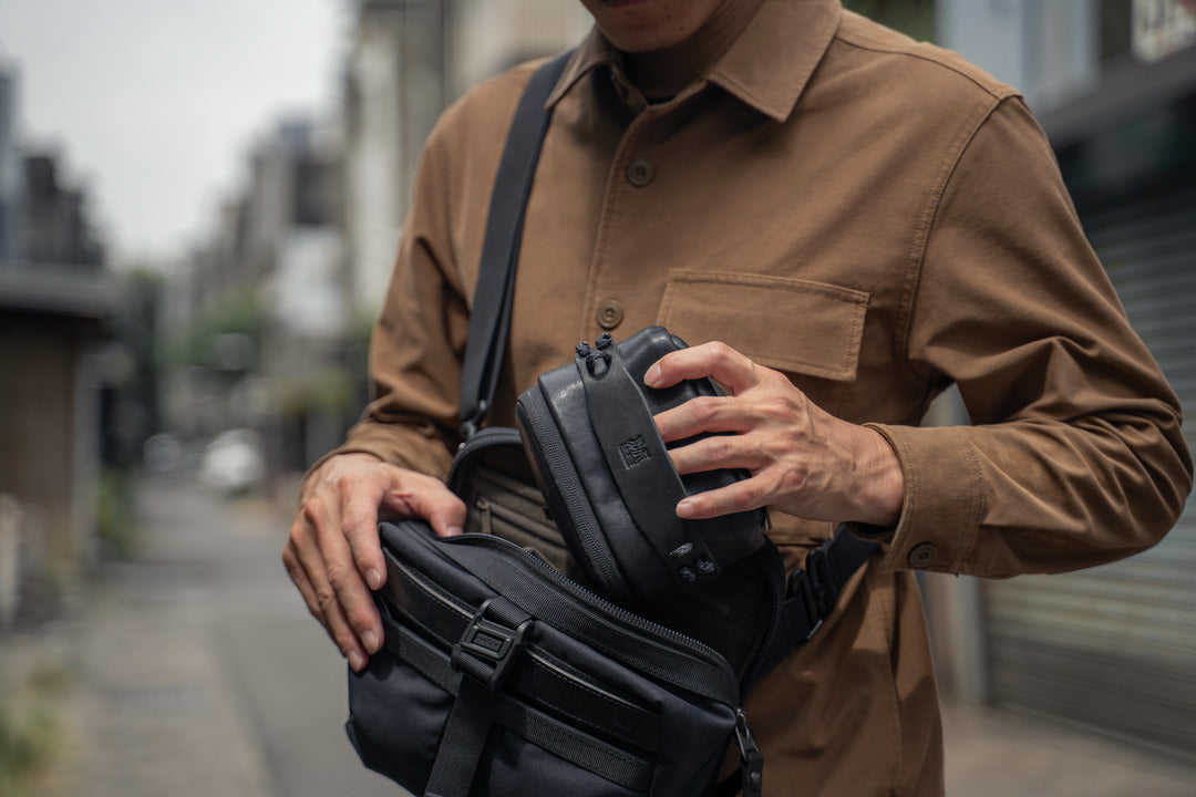 Man putting the Wotancraft black leather pouch into a larger shoulder bag