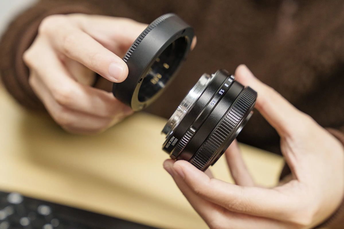TTArtisan AF 14mm f/3.5 held in hand next to its screw-on hood