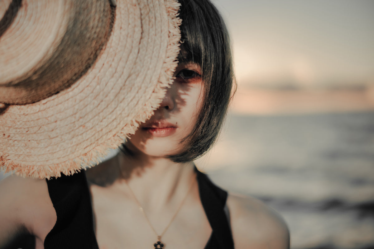 Close portrait of a woman half hidden by a straw hat, f/1.2 sample from the Voigtlander Nokton 40mm