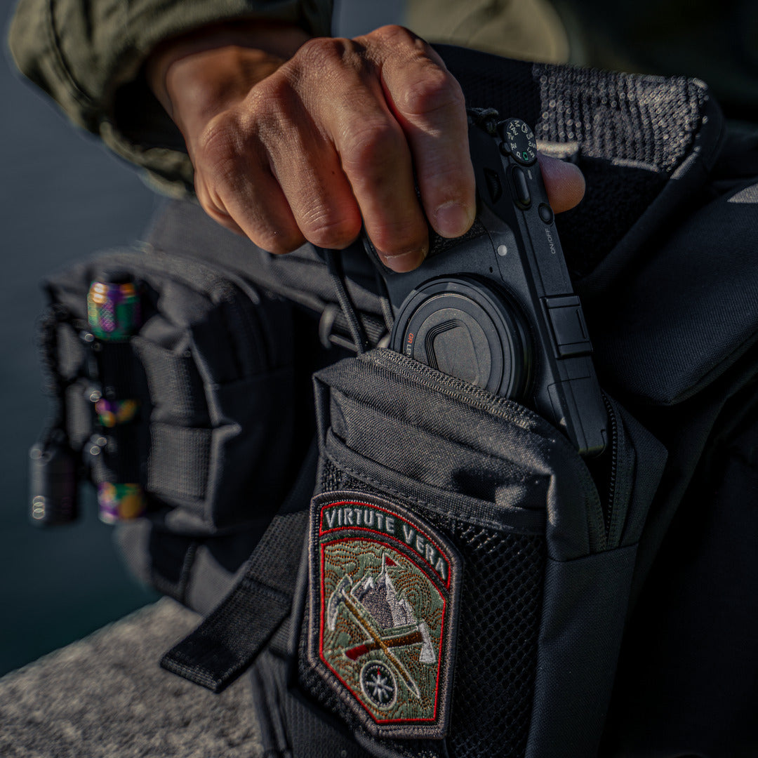 Hand putting a compact camera into a Wotancraft Armor pocket on a black bag