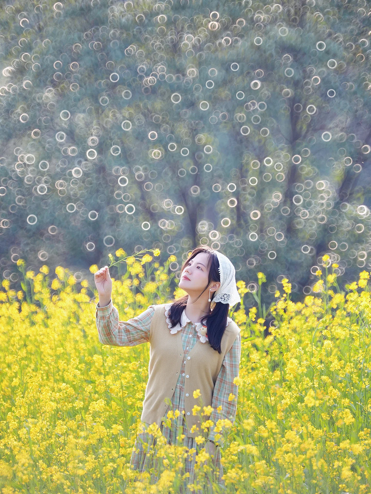Woman in a field of yellow flowers with bubble bokeh trees, TTArtisan 250mm f/5.6 sample