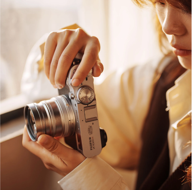 Woman holding a silver Fujifilm X100 with a Viltrox converter lens