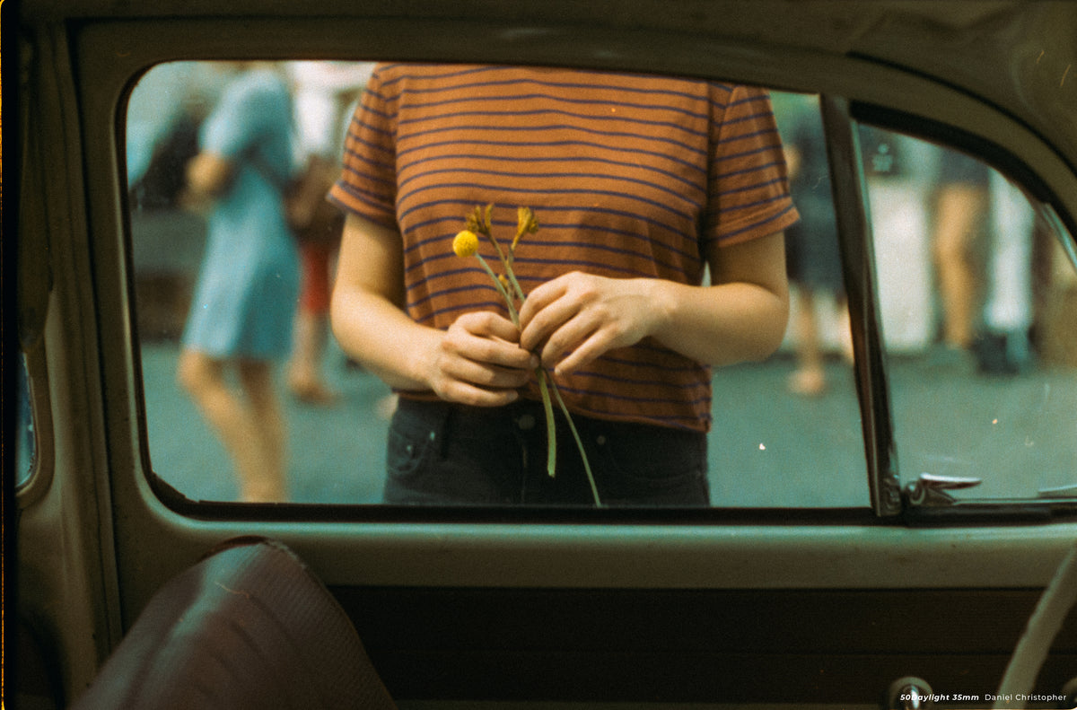 Woman holding yellow flowers outside a car window, sample shot on CineStill 50D