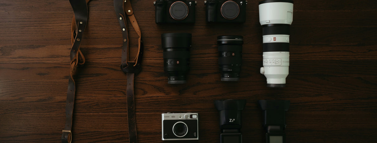 Cameras, lenses, flashes and leather straps laid out on a wooden table