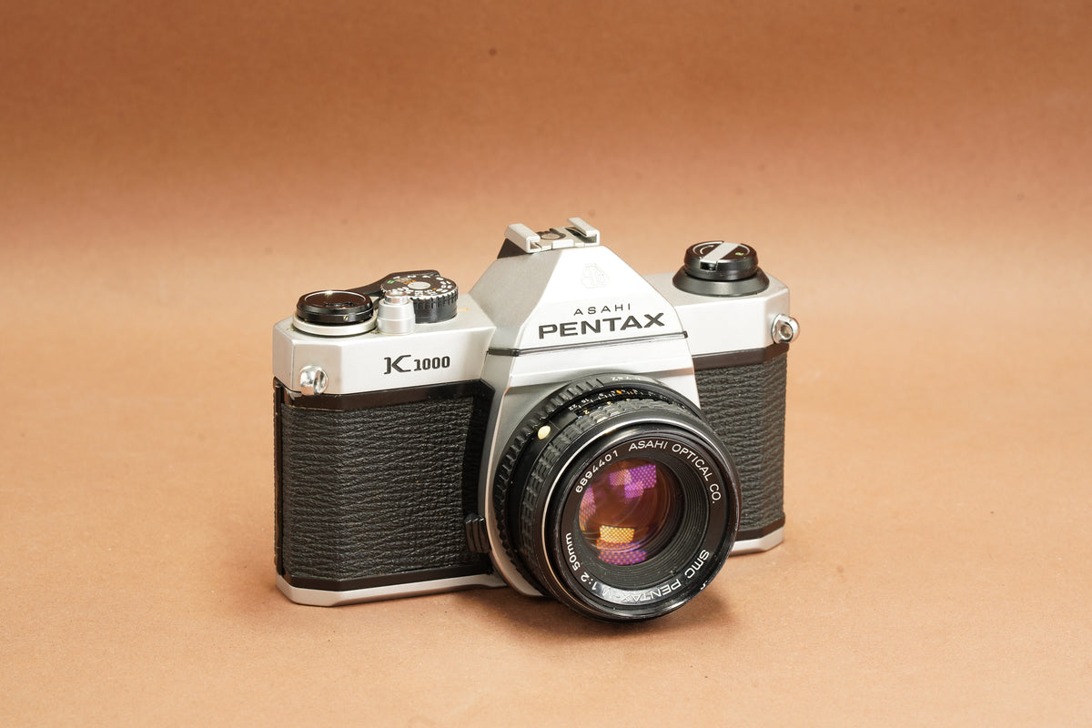 Pentax K1000 35mm SLR film camera with SMC Pentax-M 50mm f/2 lens, front three-quarter view