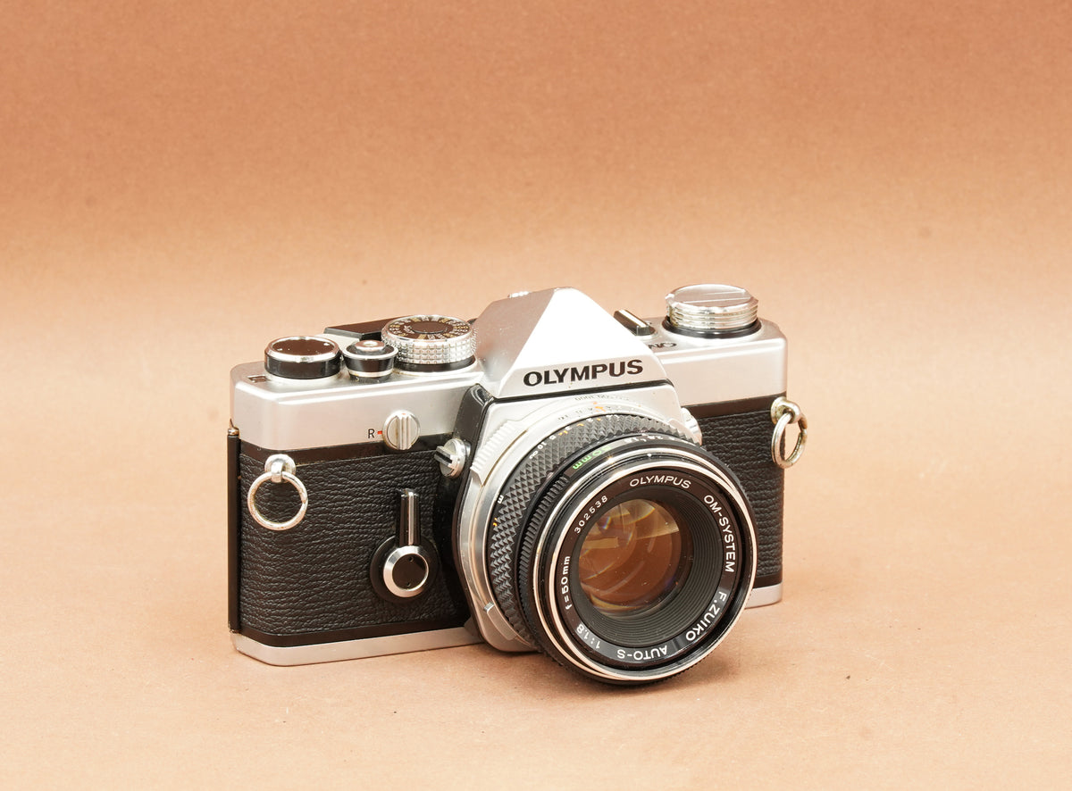 Olympus OM-1 silver 35mm SLR film camera with Zuiko 50mm f/1.8 lens, angled view