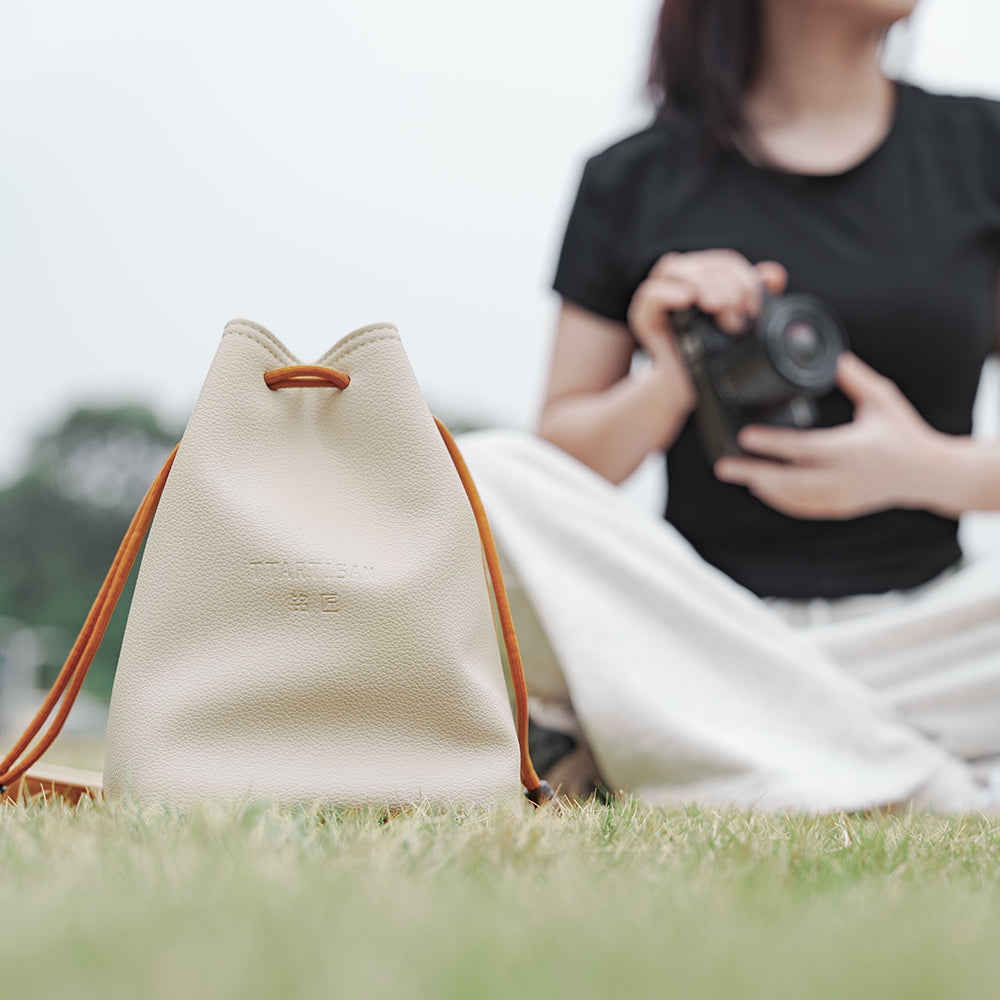 TTArtisan cream drawstring bag on grass with a woman holding a camera behind