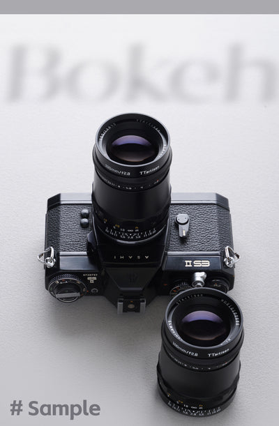 Two TTArtisan 100mm f/2.8 lenses, one fitted to an Asahi Pentax ES II film camera