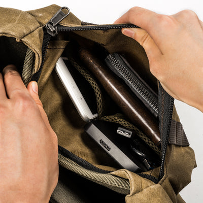 Hands opening the Wotancraft Pilot zip pocket with phone, hard drive and pen