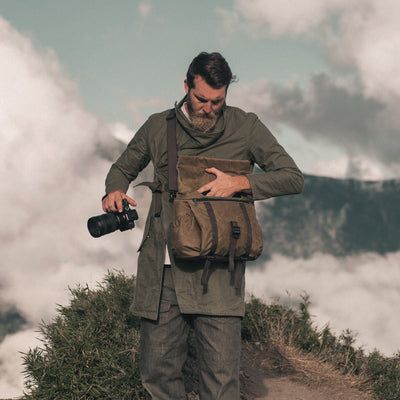 Man on a mountain path taking a camera out of the Wotancraft Pilot 10L khaki bag