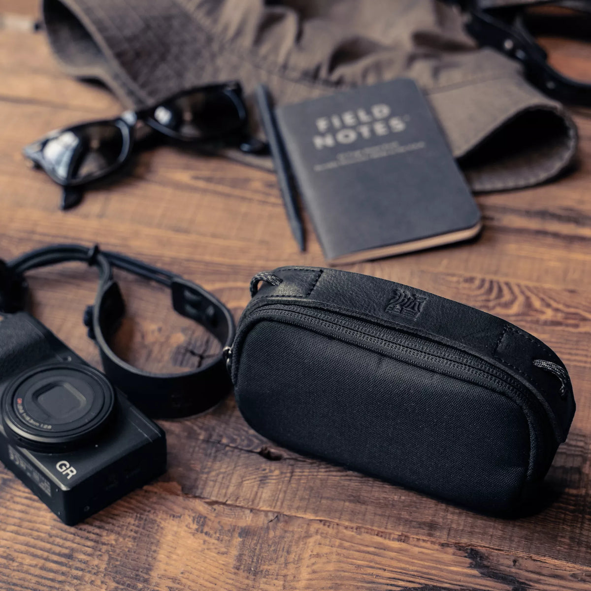 Wotancraft small black canvas pouch next to a Ricoh GR, notebook and sunglasses