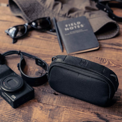 Wotancraft small black canvas pouch next to a Ricoh GR, notebook and sunglasses