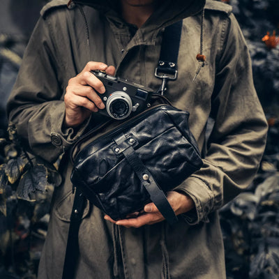 Person holding a Leica camera with the Wotancraft Mini Rider black leather sling