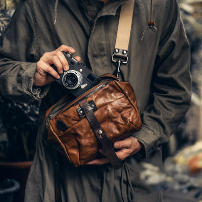 Man holding a Leica camera with the Wotancraft Mini Rider brown leather bag