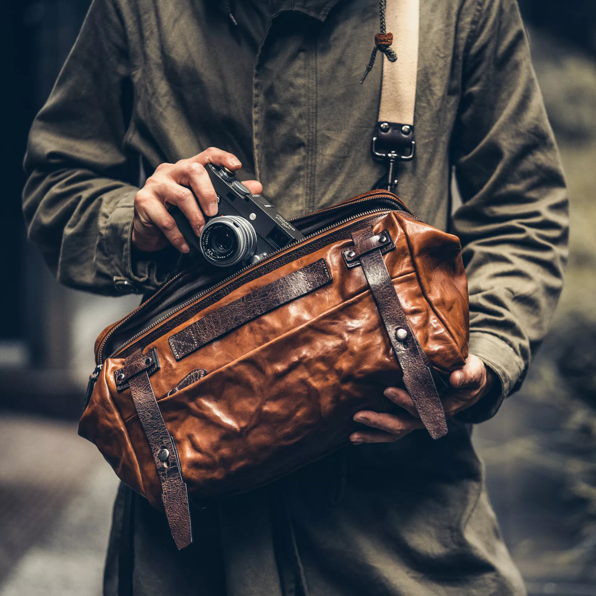 Man holding a Leica camera while wearing the Wotancraft Night Rider brown leather bag