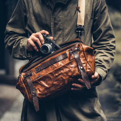 Man holding a Leica camera while wearing the Wotancraft Night Rider brown leather bag