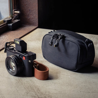 Wotancraft black canvas medium pouch next to a Leica D-Lux with brown wrist strap