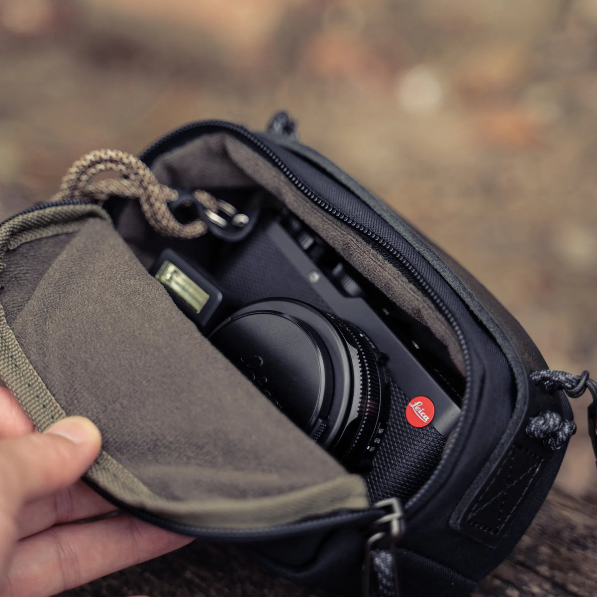 Hand opening the Wotancraft black canvas medium pouch with a Leica D-Lux inside