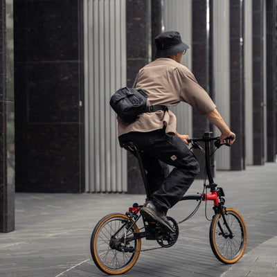 Cyclist on a folding bike wearing the Wotancraft Mini Rider v2 black sling