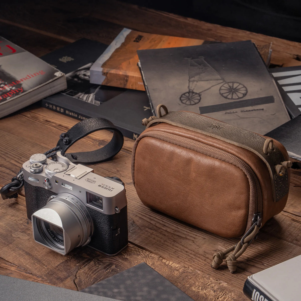 Wotancraft brown leather camera pouch beside a Fujifilm X100VI on a desk with books