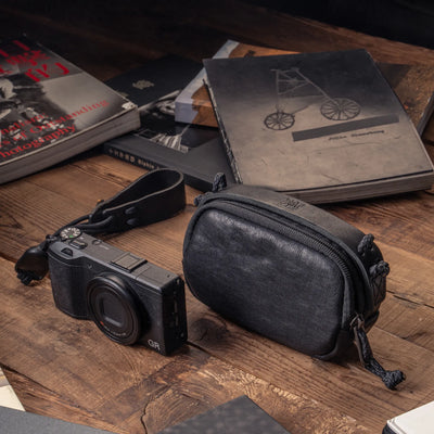 Wotancraft black leather small pouch next to a Ricoh GR on a desk with photo books