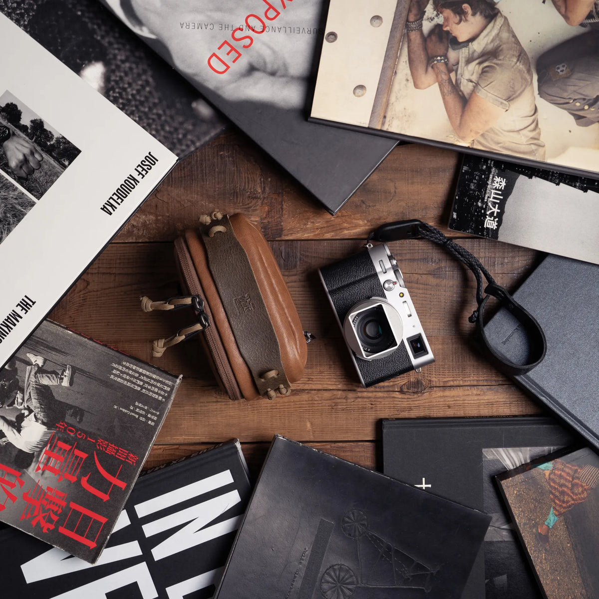 Wotancraft brown leather pouch open and a Fujifilm X100 among photo books, from above