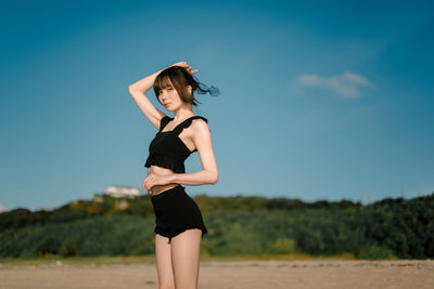 Woman in black posing on a beach under blue sky, sample from the Voigtlander Nokton 40mm f/1.2