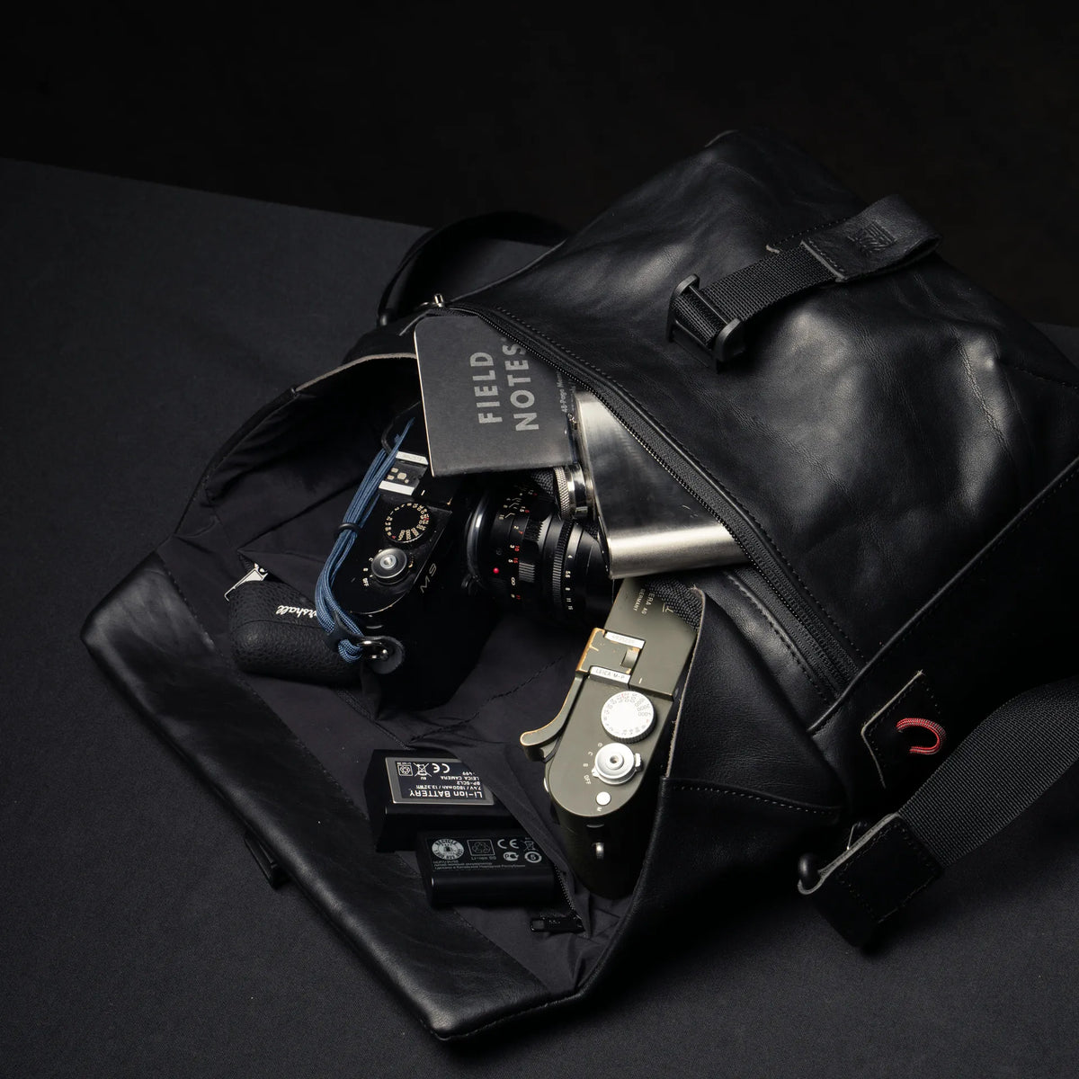 Wotancraft Pilot black leather bag open with Leica cameras, notebook and batteries
