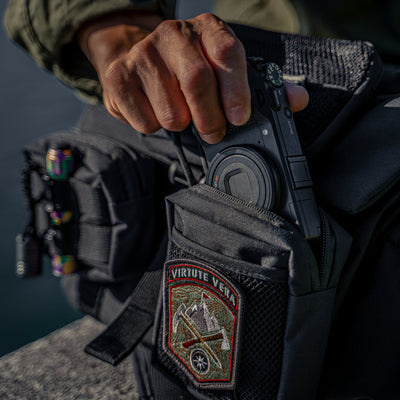Hand putting a compact camera into a Wotancraft Armor pocket on a black bag