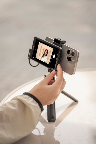 Hand holding a tripod grip with an iPhone and the Viltrox DC-T1 monitor for selfie framing