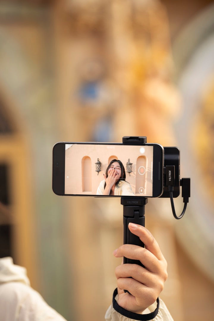 Hand holding an iPhone with the Viltrox DC-T1 on a grip, woman on screen