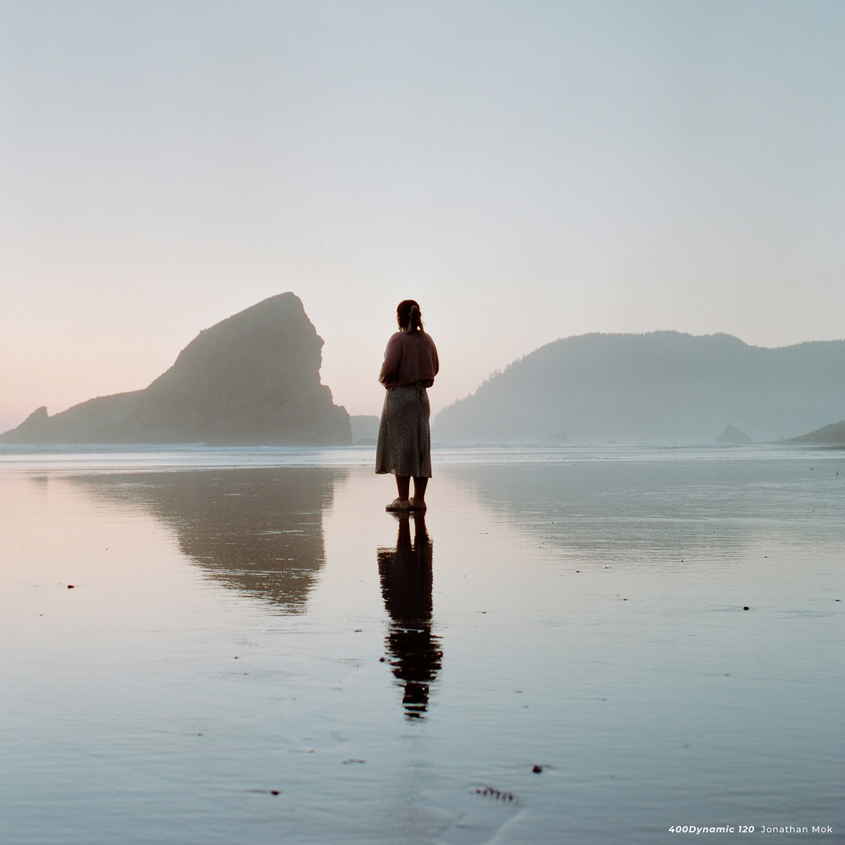 Woman standing on a wet beach at dusk with sea stacks, sample shot on CineStill 400D