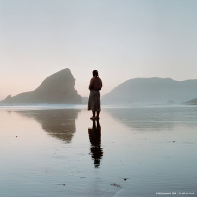Woman standing on a wet beach at dusk with sea stacks, sample shot on CineStill 400D