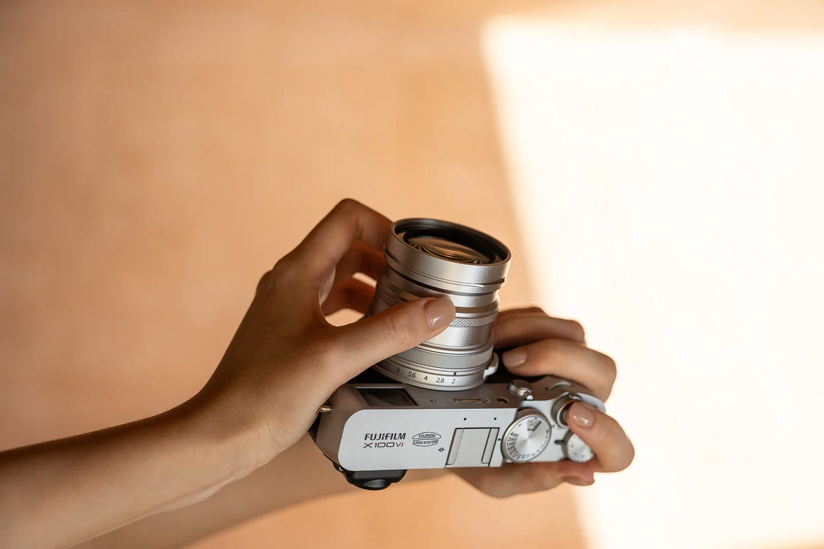 Hands holding a silver Fujifilm X100 with a Viltrox converter lens