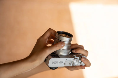 Hands holding a silver Fujifilm X100 with a Viltrox converter lens