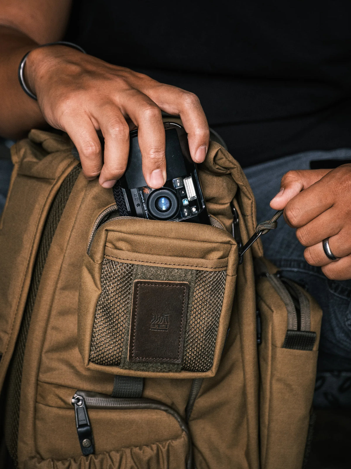 Hand putting a compact camera into a Wotancraft brown Armor pocket on a backpack