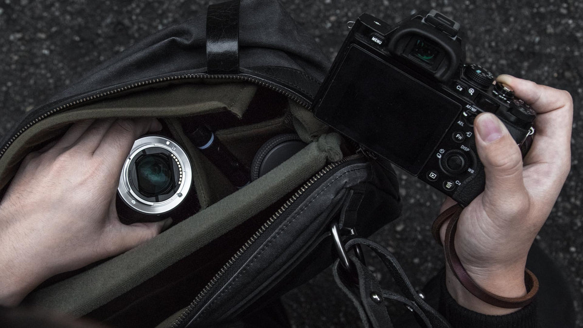 Hands taking a lens and Sony camera out of a Wotancraft bag with insert