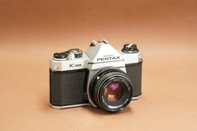 Pentax K1000 35mm SLR film camera with SMC Pentax-M 50mm f/2 lens, front three-quarter view